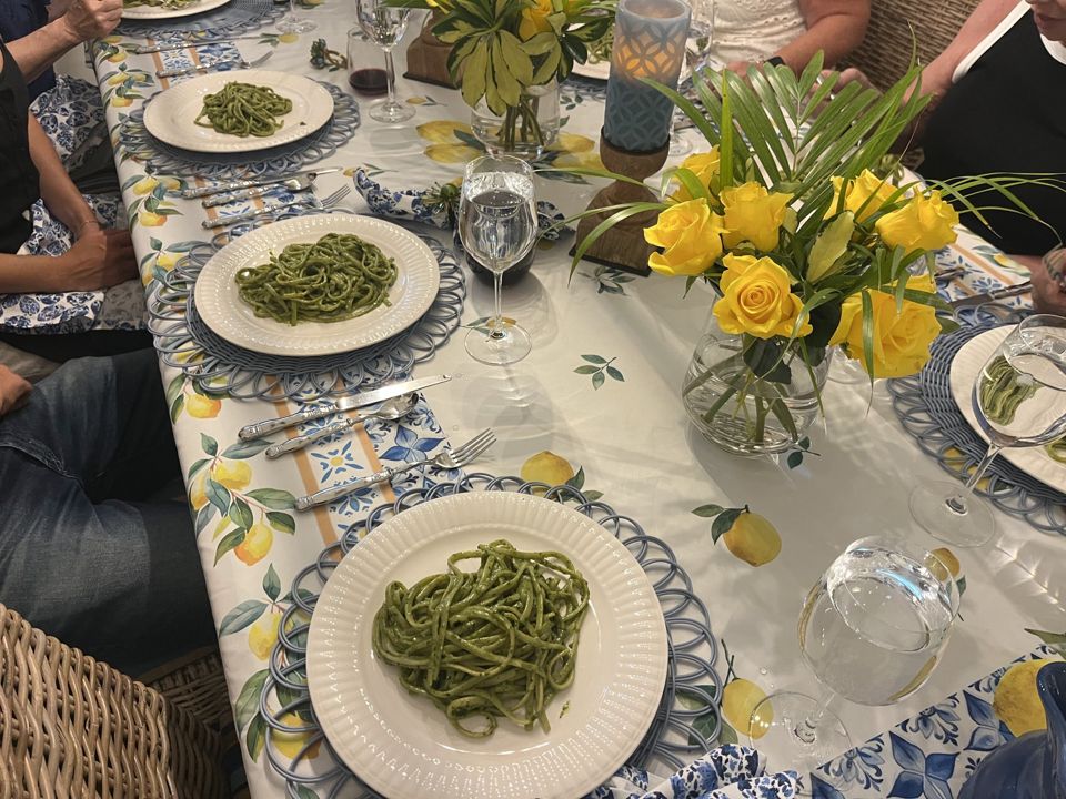 A long dinner table set with plates of pesto linguine and yellow roses